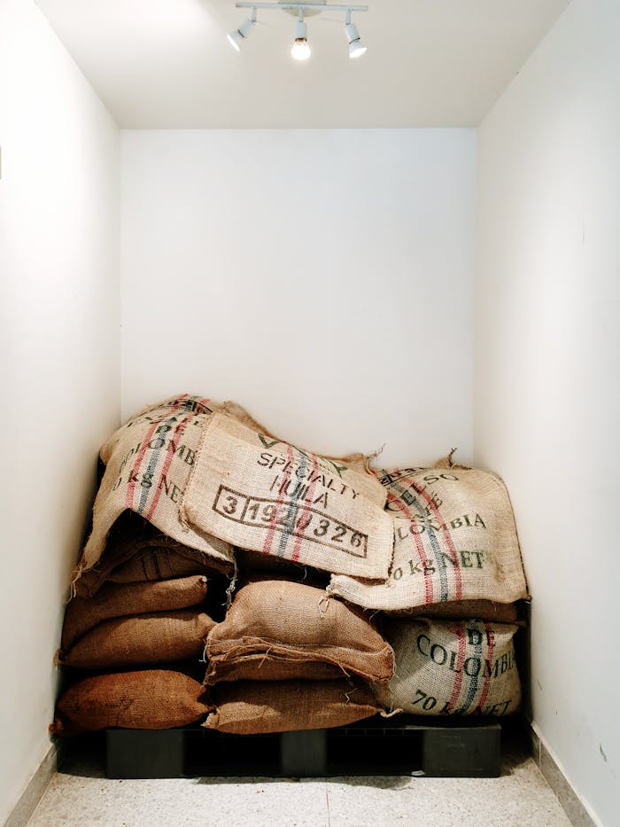 Burlap coffee sacks stacked in a small, well-lit warehouse corner, ready for distribution.